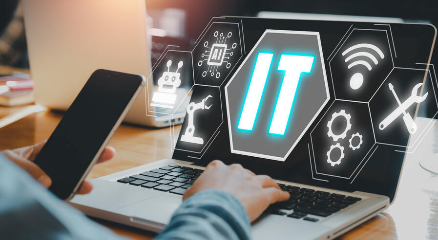 Symbolbild für einen Mitarbeiter, der am PC arbeitet und parallel am Handy arbeitet. Es sind nur die Hände der Person zu sehen.