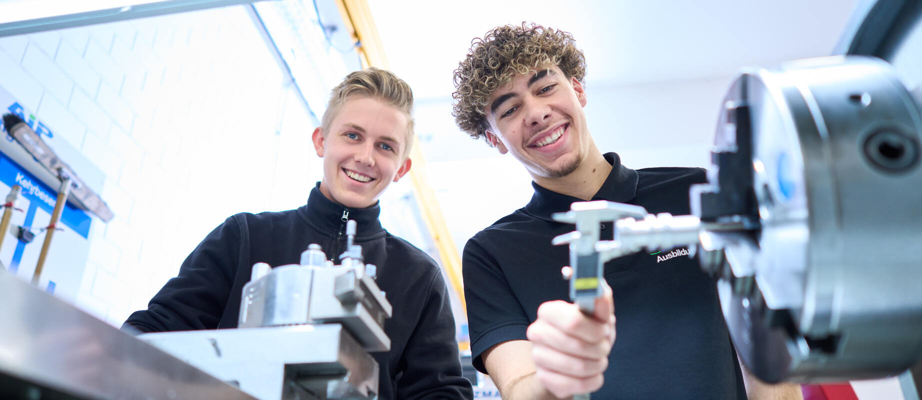 Zwei Auszubildende arbeiten gemeinsam an der Drehmaschine und lachen dabei.