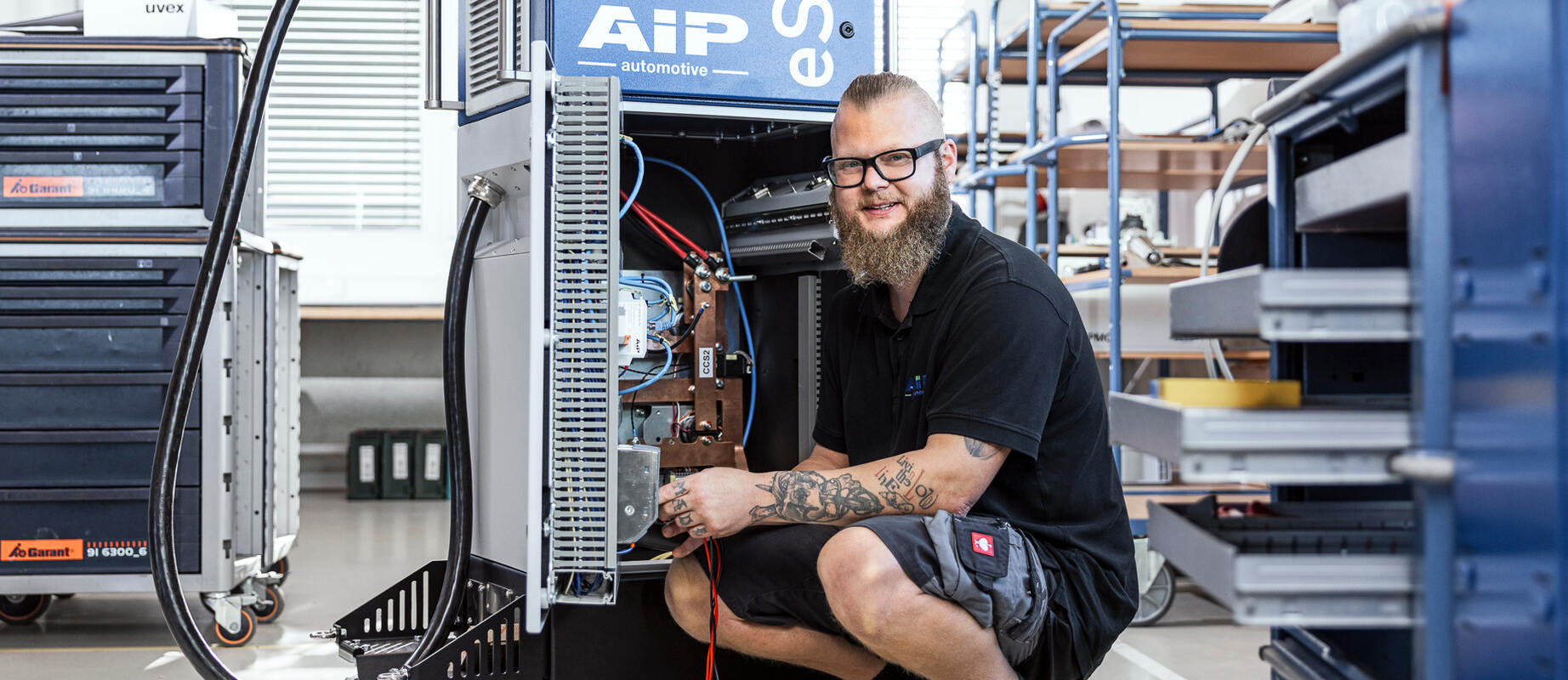 Ein Mitarbeiter arbeitet an einer E-Ladesäule und schaut lachend in die Kamera.