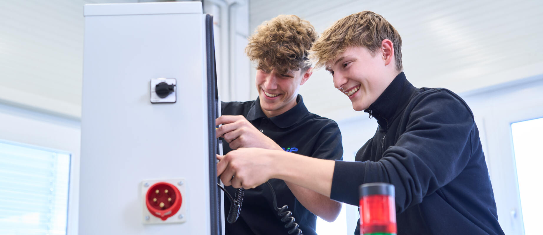 Zwei Auszubildende arbeiten gemeinsam an einem Schaltschrank.