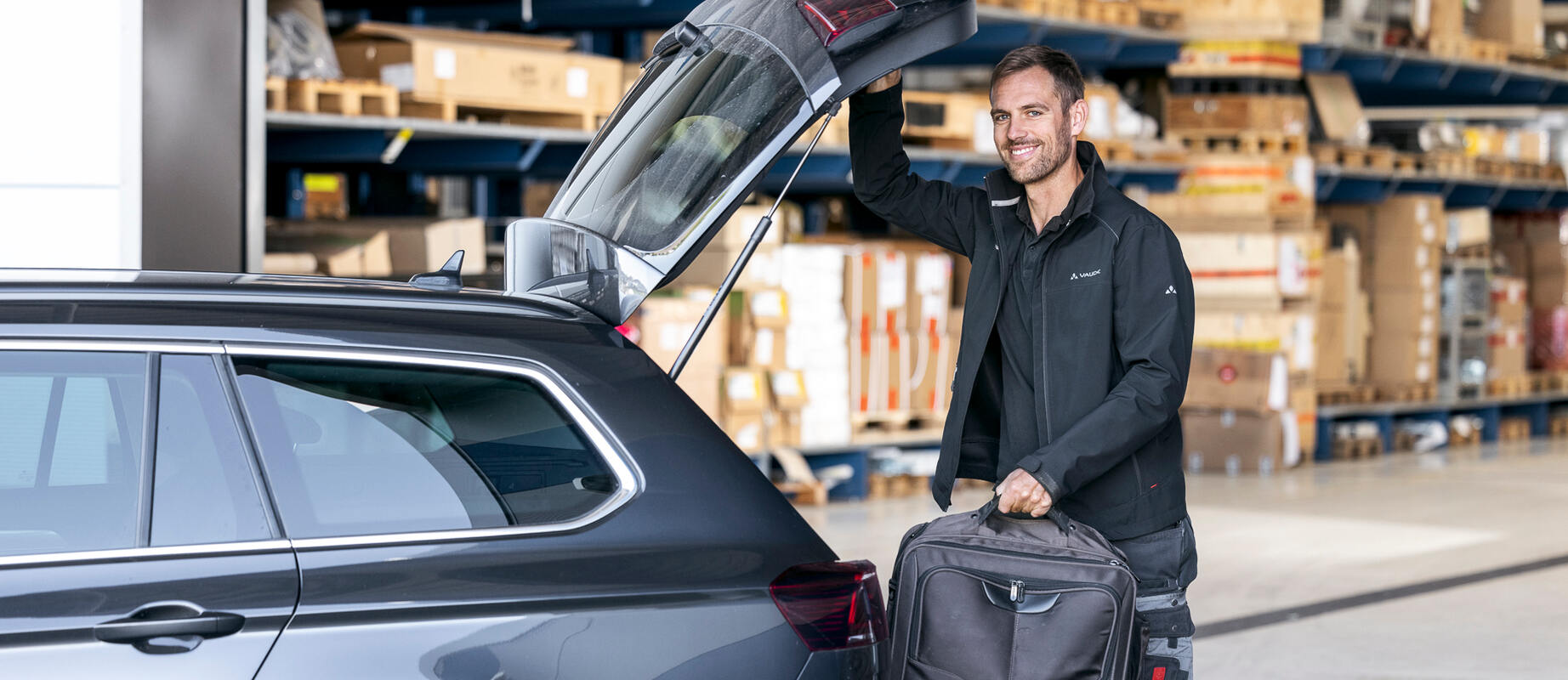 Außendienstmitarbeiter lädt seine Tasche in seinen Dienstwagen und lächelt in die Kamera