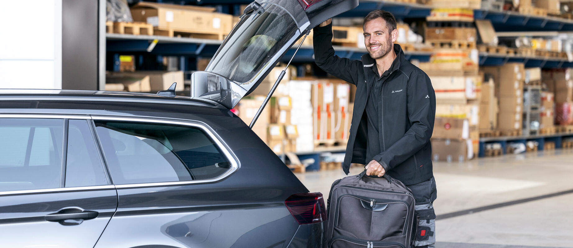 Außendienstmitarbeiter lädt seine Tasche in seinen Dienstwagen und lächelt in die Kamera