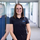 Mitarbeiterin lehnt an der Wand und lächelt in die Kamera.