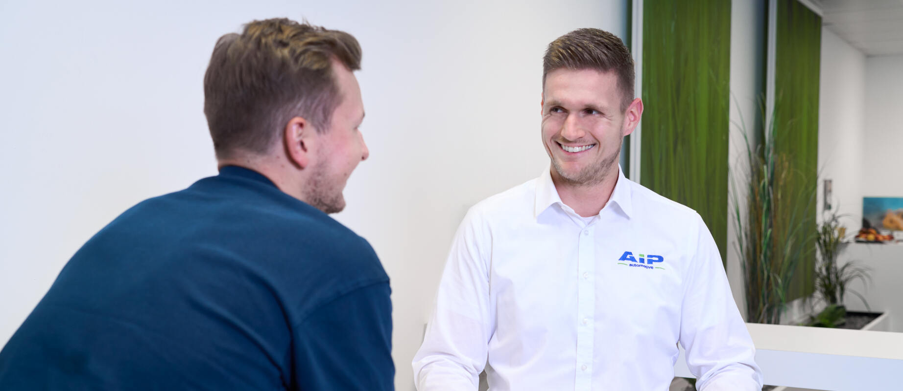 Servicemitarbeiter lächelt einen Kunden an, den man von hinten erkennt.