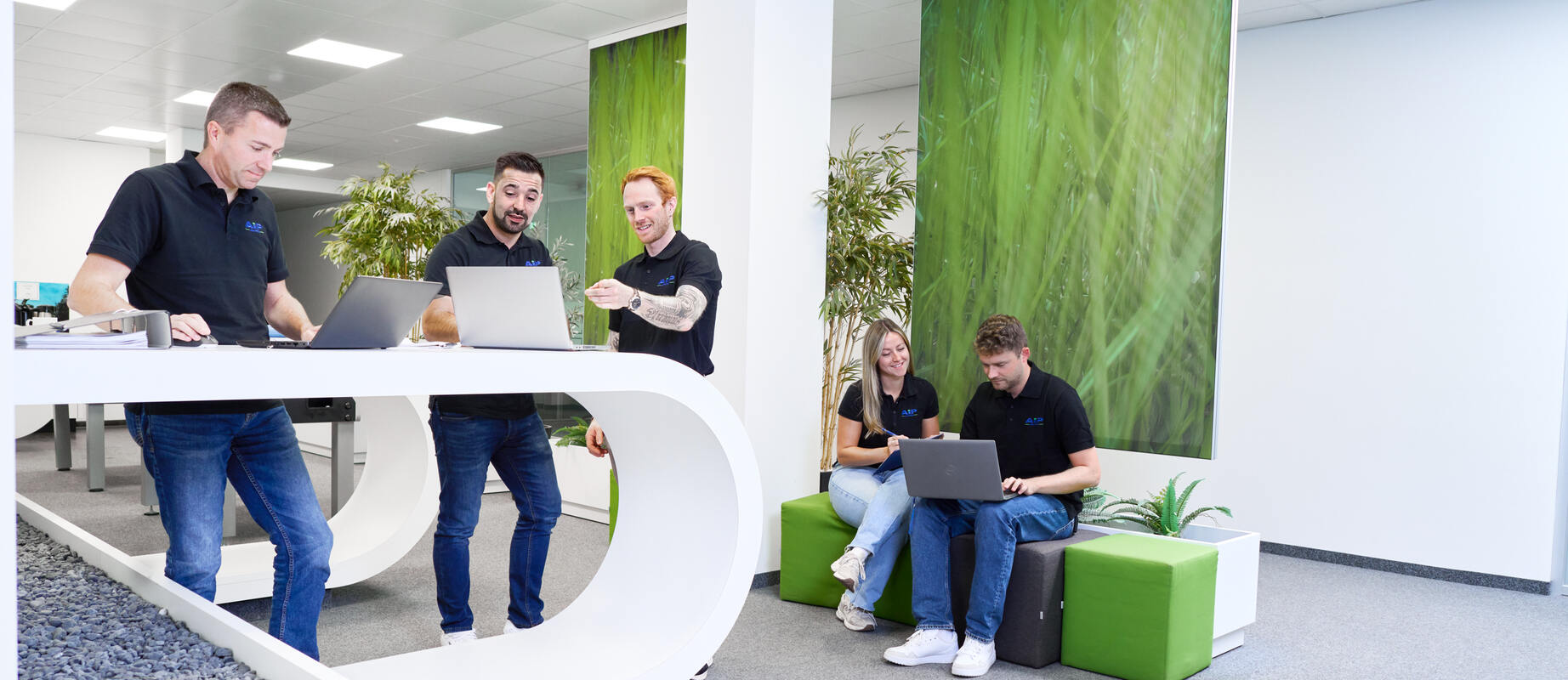 Fünf Mitarbeitende halten sich in einer Lounge auf und arbeiten in Kleingruppen.