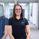 Mitarbeiterin lehnt an der Wand und lächelt in die Kamera. 